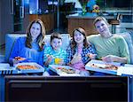 Family eating pizza in front of television in living room