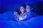 Mother and children using digital tablet in bed