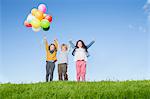 Children with balloons cheering on grassy hill