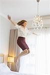 Businesswoman jumping on bed in hotel room