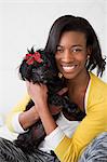 A young girl smiling, holding her small black pet dog.