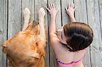 A young girl and a golden retriever dog side by side on a jetty.