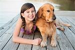 A young girl and a golden retriever dog lying on a jetty.