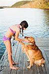 A girl in a bikini with a golden retriever dog lifting its paw up.