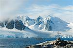 A cross and grave on a hilltop overlooking the snow capped peaks of the mountains on Petterman island. A tall masted ship in the channel.