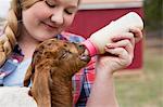 A girl bottle-feeding a baby goat.