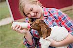 A girl bottle-feeding a baby goat.