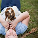 A girl cuddling a baby goat lying on her chest.