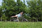 A young boy falling off his bicycle, overbalancing in a grassy field.