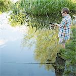 A young boy standing in water fishing with a rod.