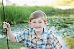 A young boy with his fishing road, by a lake or river.