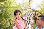 A young girl sitting on a tree trunk beside her father.