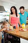 Mid adult parents watching daughter tempted by pancakes at breakfast bar