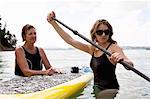 Senior woman and daughter wading with paddleboard at sea