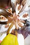 Worms eye view of seven business women and men in a circle holding hands in office