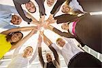 Worms eye view of seven business men and women in a circle holding hands in office