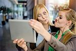 Two young businesswomen pulling faces and taking selfie on digital tablet in office
