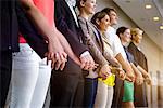 Row of businesswomen and men holding hands in office