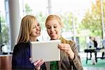Two young businesswomen pulling faces and taking self portrait on digital tablet in office