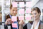 Businessman and woman arranging post it notes on office window