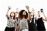 Studio portrait of five young adults taking selfies on smartphones