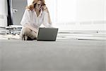 Mid adult businesswoman using laptop on floor in new office
