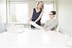 Two businesswoman looking at blueprint design in conference room