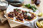 Middle eastern lamb and chickpea pizza with herb garnish and lemon slices