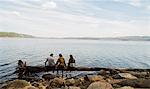 Three hiking friends sitting in a row on fallen tree at lakeside