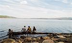 Three hiking friends sitting in a row on fallen tree at lakeside