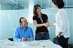 Architect greeting client with blueprints on boardroom table