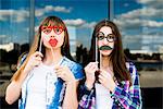 Portrait of two young women holding up lip and eye costume masks