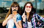 Portrait of two young women holding up mustache and eyeglass costume masks