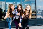 Three young women leaning forward in a row and making I love you hand gesture