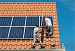 Workers installing solar panels on roof framework of new home, Netherlands