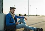 Young man with smartphone waiting in empty parking lot