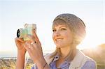 Young woman taking photograph with camera at sunset