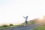 Young woman taking photograph on hill at sunset