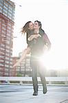 Mid adult man giving girlfriend piggyback on rooftop parking lot