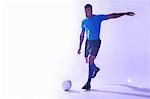 Studio shot of young male soccer player kicking the ball