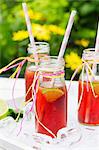 Three small bottles of iced tea with lime, peppermint and ice cubes on a garden table