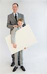 Father and son holding blank whiteboard, smiling, portrait