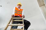 Portrait of construction worker with safety helmet standing on a ladder at construction site of new building