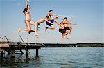 Five teenagers jumping from a jetty into lake