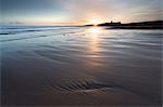 View over Embleton Beach at sunrise towards the silhouetted ruin of Dunstanburgh Castle in the distance, Embleton Bay, near Alnwick, Northumberland, England, United Kingdom, Europe