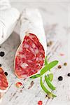 White sausage fuet with fresh herbs and colorful peppercorns on white textured wooden background. Traditional spanish meat.