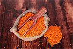 Red lentils in burlap sack on wooden spoon on dark wooden background, top view. Healthy eating.