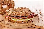 Whole grain bagel with bacon on wooden kitchen board on wooden background. Traditional bagel eating.