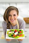 Portrait of smiling young housewife showing greek salad