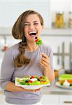 Happy young woman eating greek salad in kitchen